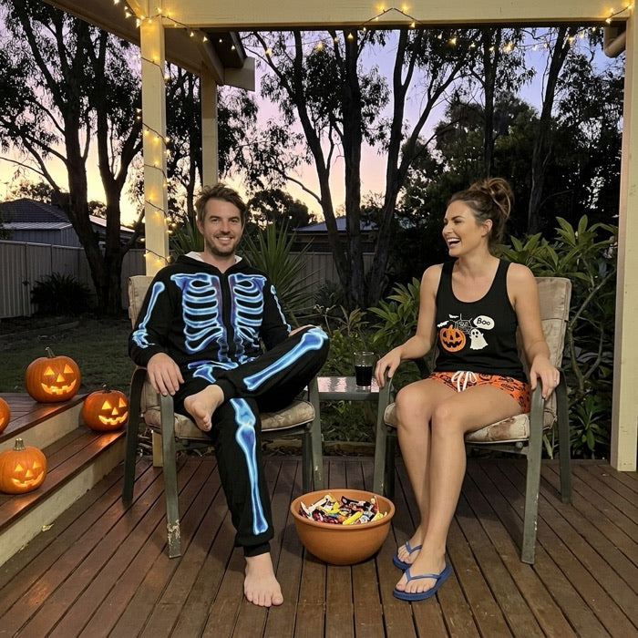 Couple on a veranda in skeleton and pumpkin Halloween pyjamas handing out sweets