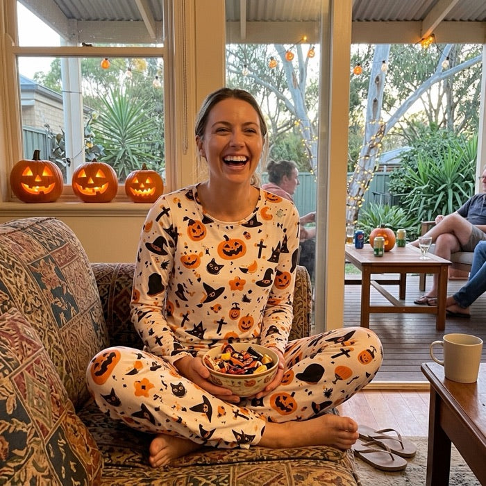 Woman in pumpkin print Halloween pyjamas on the sofa with a bowl of sweets